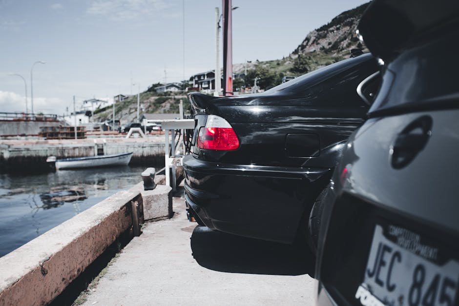Close-up of classic black cars parked by a peaceful waterfront harbor on a sunny day