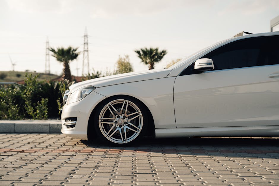 Side view of a white luxury car parked on a sunny day with palm trees in the background