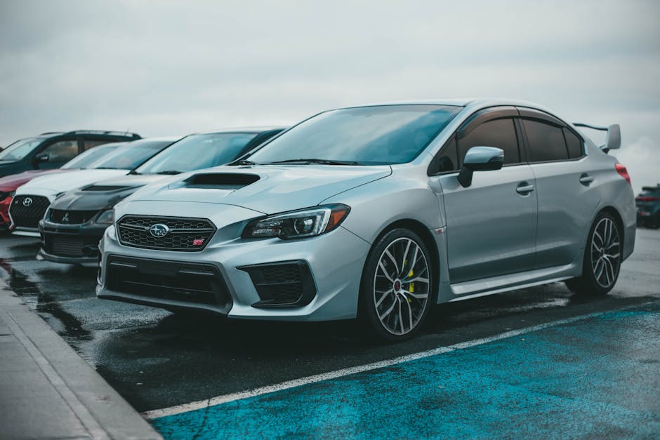 A silver Subaru WRX parked in a city parking lot with other cars on a rainy day