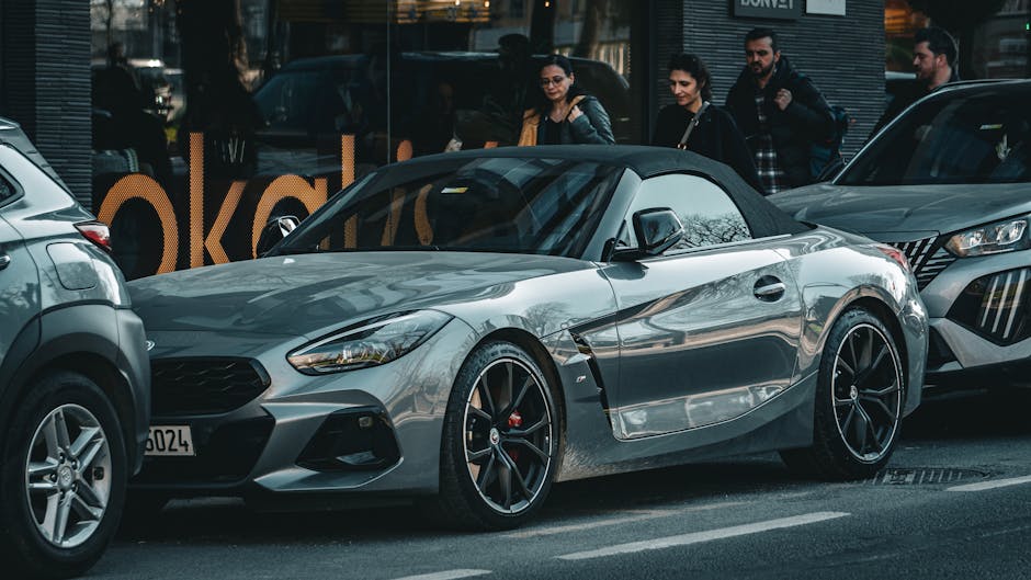 Gray BMW Z4 roadster parked on a bustling city street with people passing by, capturing urban lifestyle