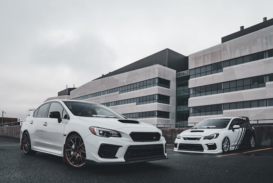 Two tuned white Subaru WRX sports cars parked in a modern urban environment with building backdrop