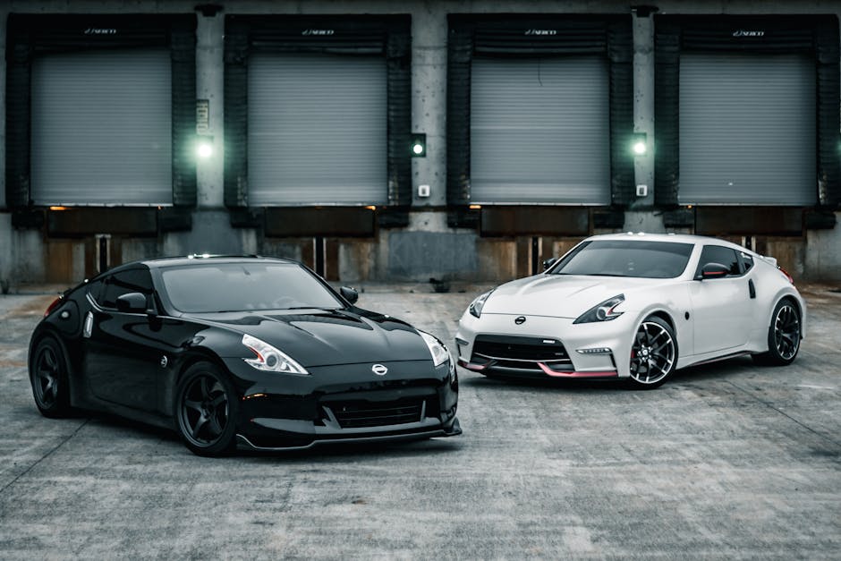 Contemporary luxury black and white sports cars parked near gates of industrial loading zone in daytime