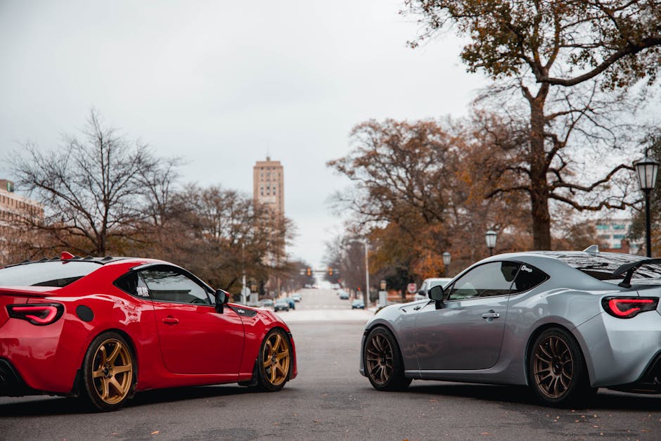 Two luxury sports cars parked on an urban street with trees and buildings in the background